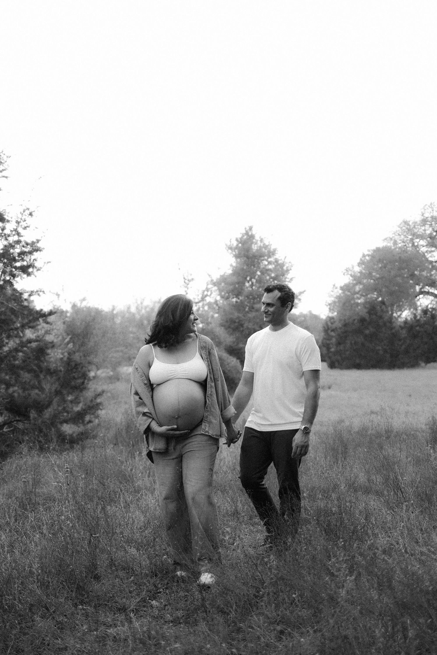 A couple walks together through a misty meadow in black and white, creating a romantic vintage scene. maternity, baby bump