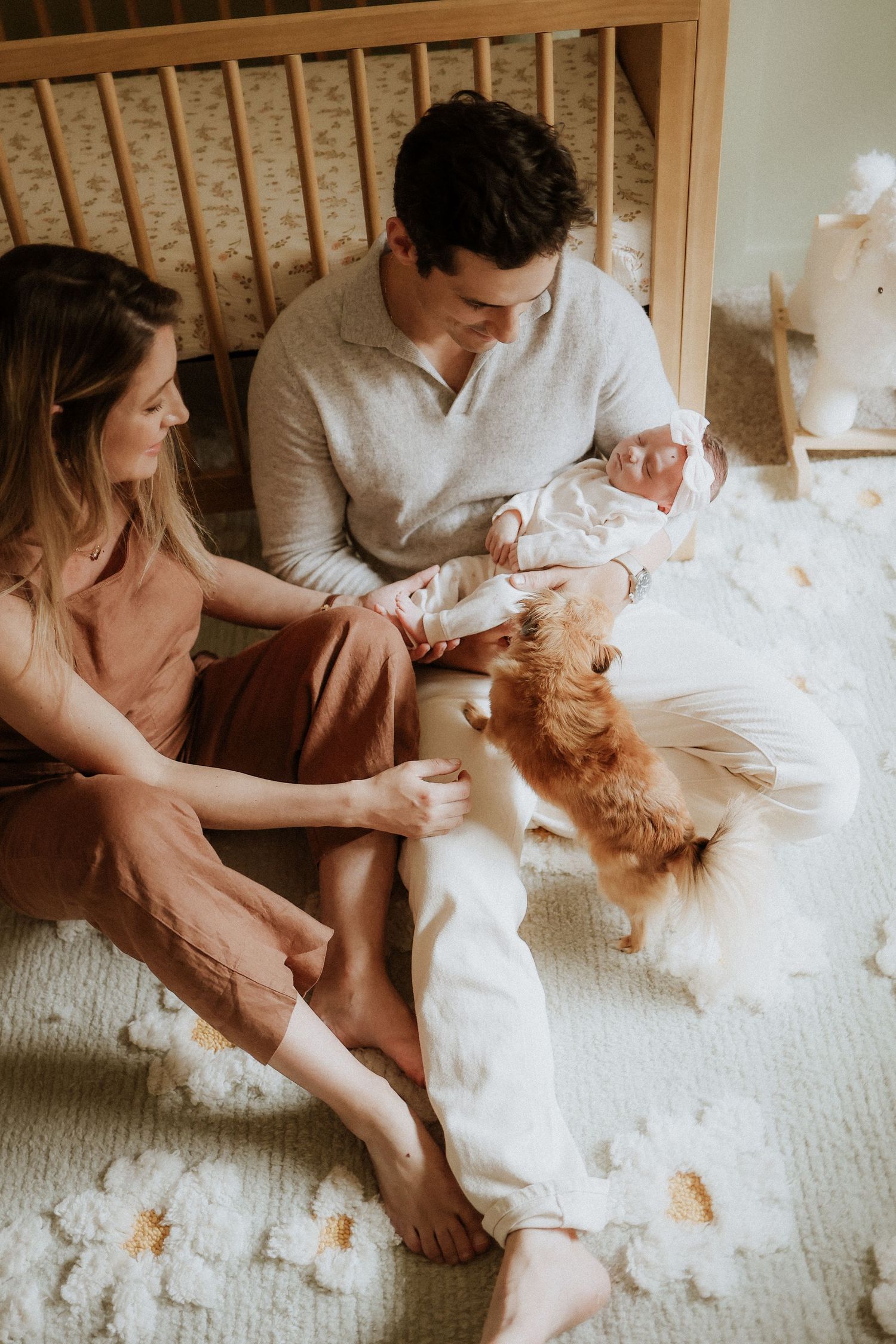 A couple sits on a carpeted floor playing with their fluffy white dog who is shedding fur everywhere. newborn, nursery, family portrait