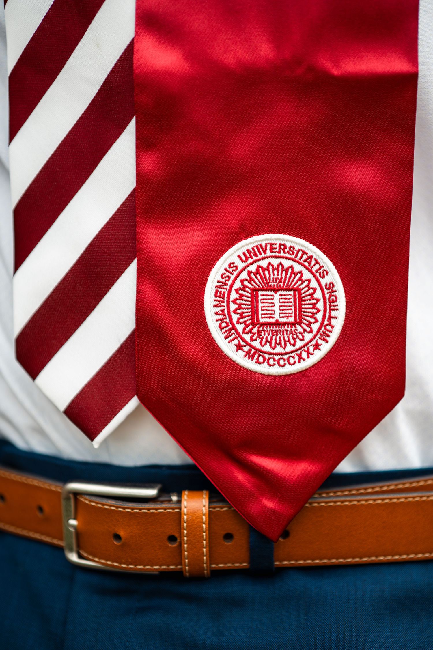 Closeup portrait of Indiana University graduate wearing IU stole and red candy stripe tie, formal graduation attire.