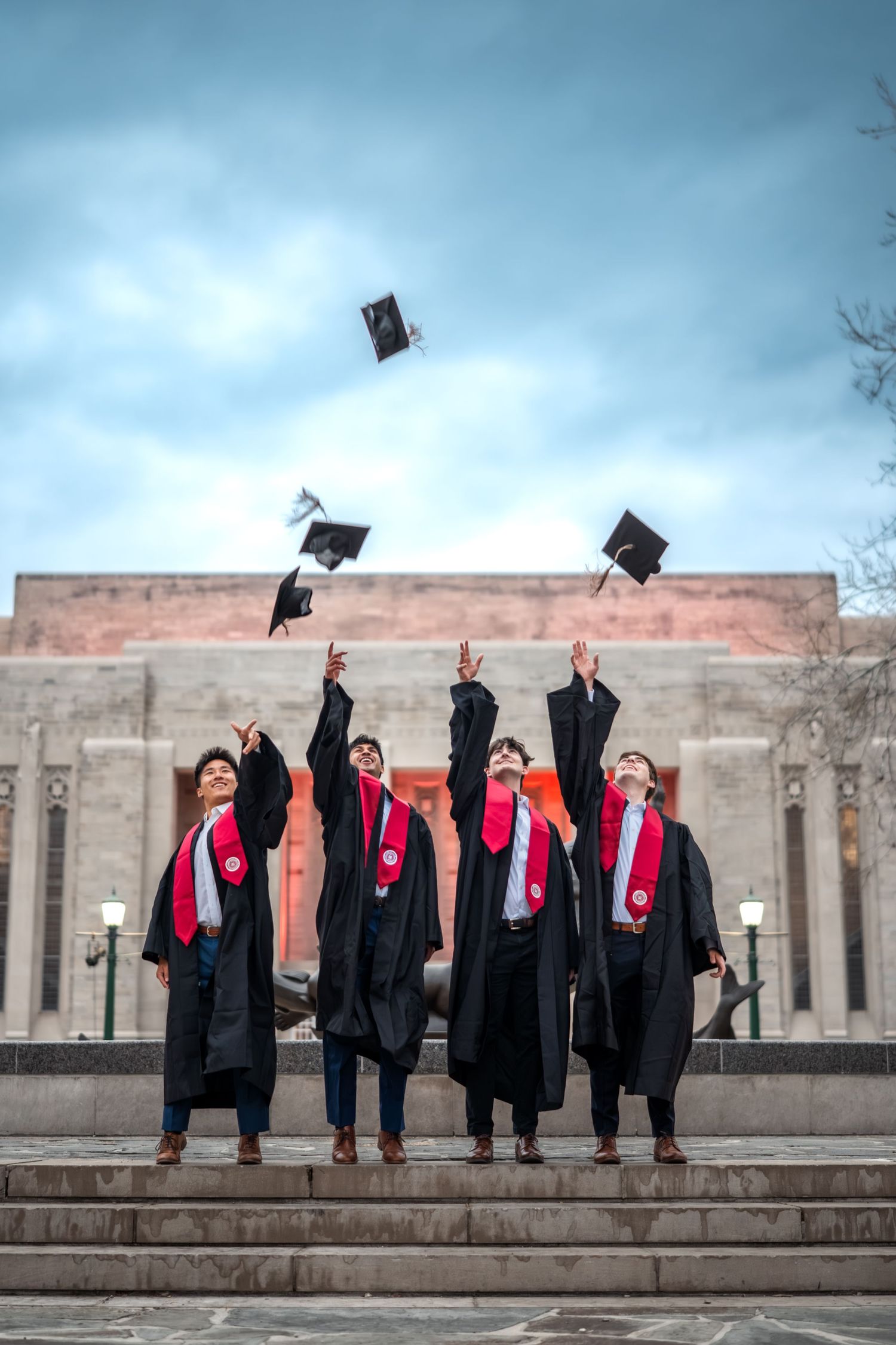 Group of Indiana University graduates tossing caps in the air at Showalter Fountain on IU Bloomington campus during graduation photo session
