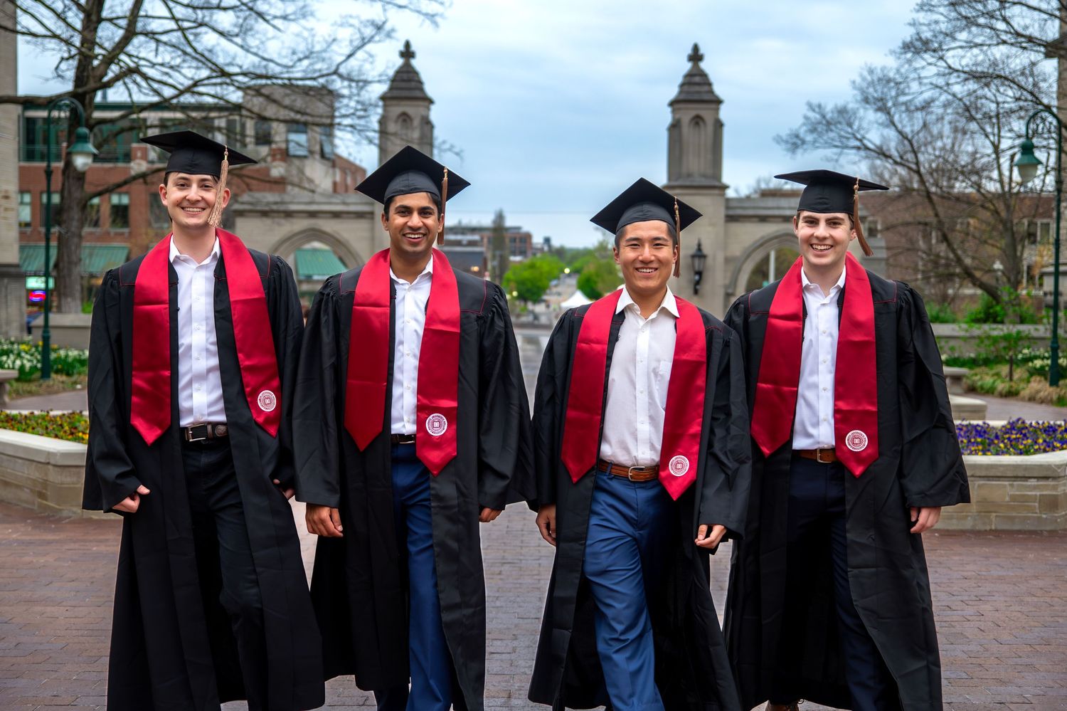 group of Indiana University graduates in caps and gowns walking and smiling on IU Bloomington campus during grad photo session