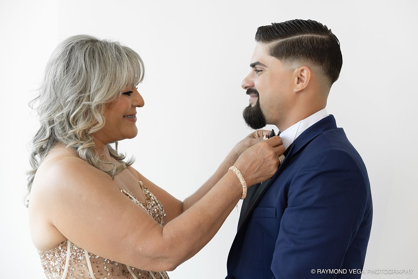 Older woman with gray hair adjusting a young man's boutonniere as he wears a navy blue suit at a wedding. Hotel la Concha Wedding