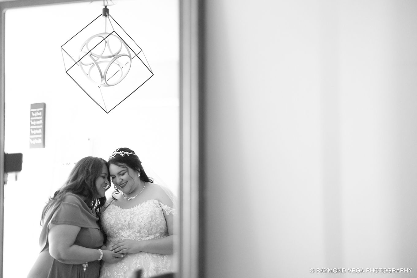 Black and white photo of bride and bridesmaid sharing an intimate moment, smiling together before the wedding ceremony.