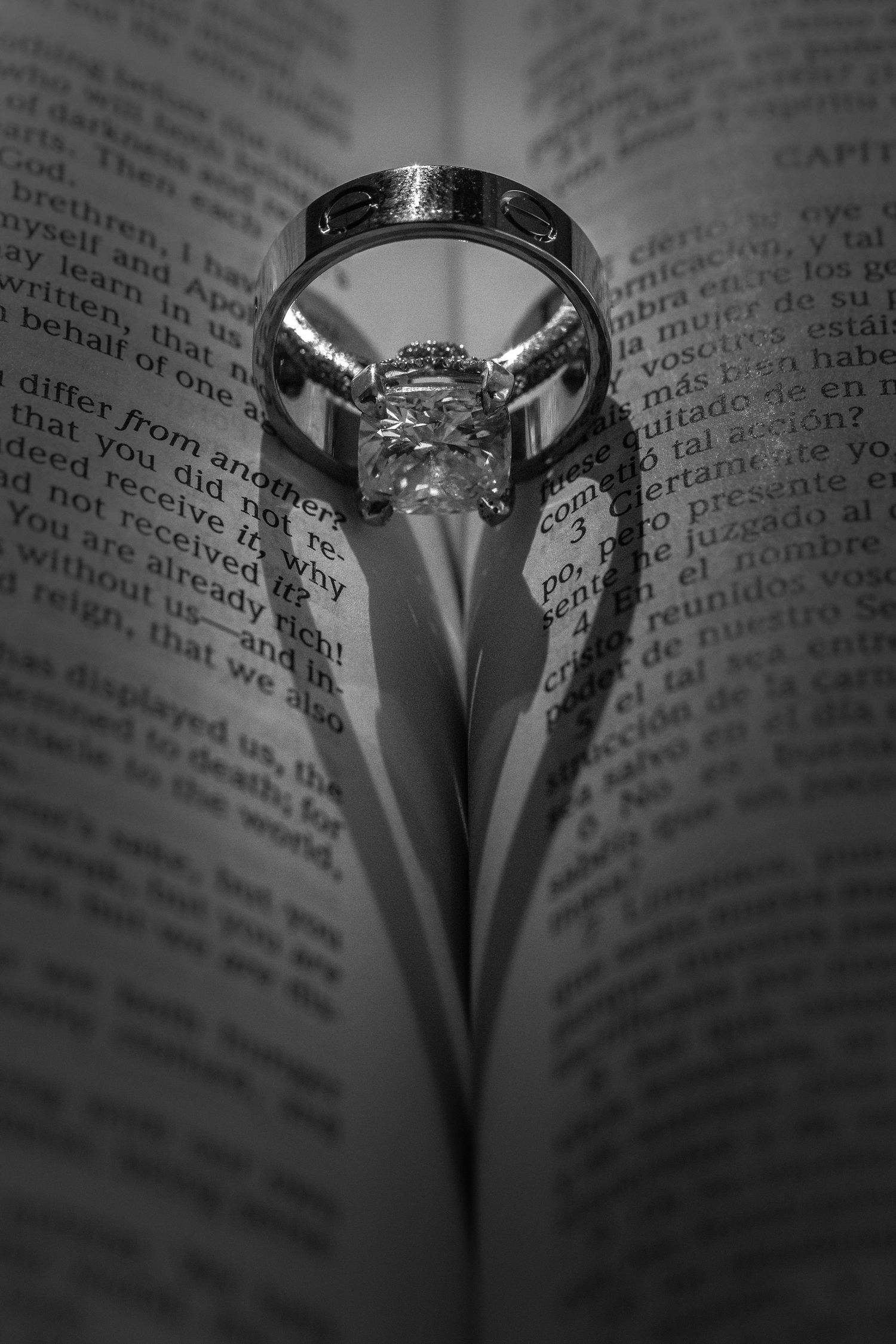 Black and white photo of a diamond engagement ring casting a heart-shaped shadow on an open Bible.