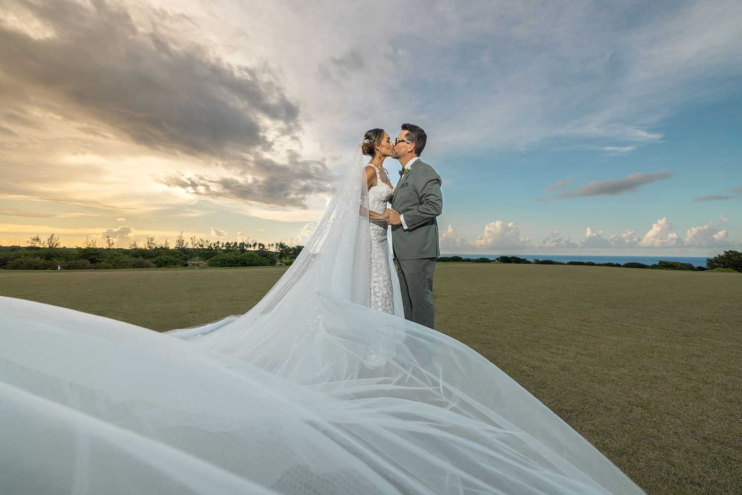 Bride and groom kiss in open field with dramatic sky and flowing veil — award-winning destination wedding photographer Puerto Rico