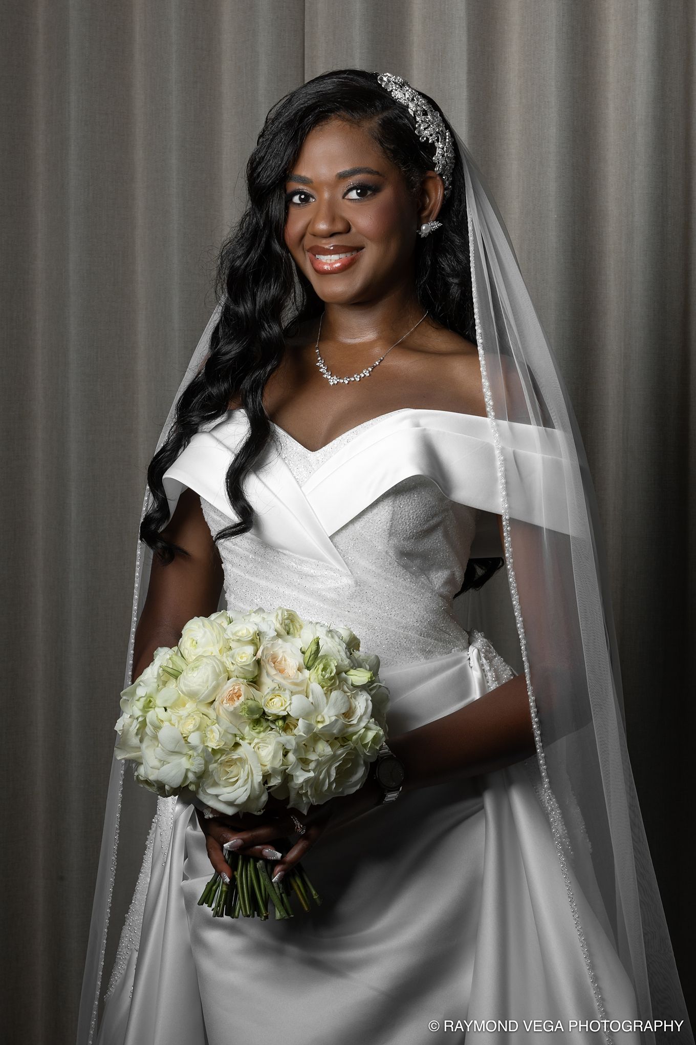 Elegant bride in white off-shoulder gown with veil, tiara, and bouquet of white roses, smiling beautifully. Hotel Condado Vanderbilt