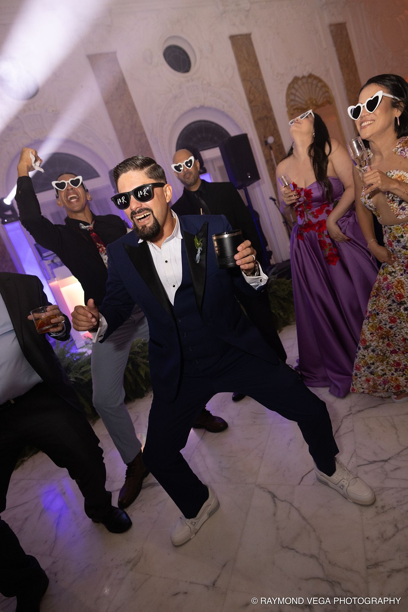 Groom in navy suit and novelty sunglasses dancing joyfully with guests at a lively wedding reception.Antiguo Casino Puerto Rico wedding