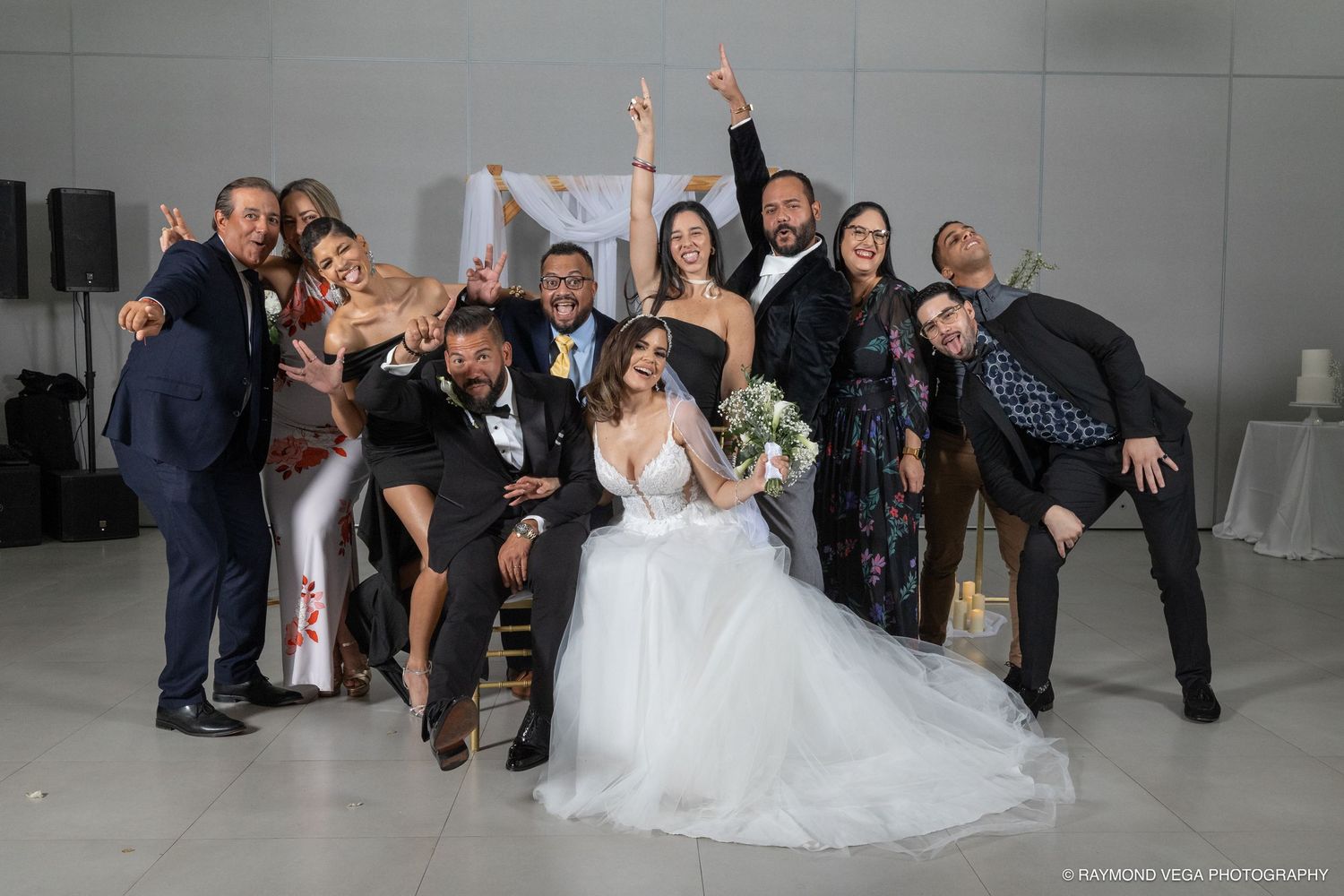 Wedding party celebrates with bride and groom in elegant venue, guests posing joyfully in formal attire.
