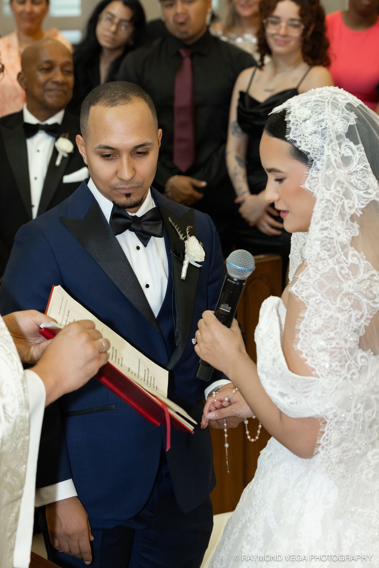 Bride reads vows into microphone while groom listens attentively during elegant church wedding ceremony.