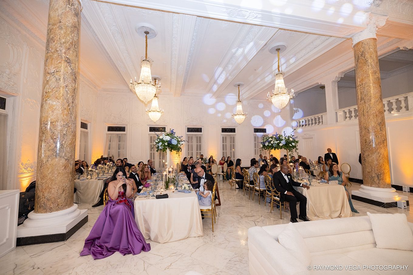 Elegant wedding reception in a grand ballroom with chandeliers, marble columns, and guests seated at decorated tables.Antiguo Casino Puerto