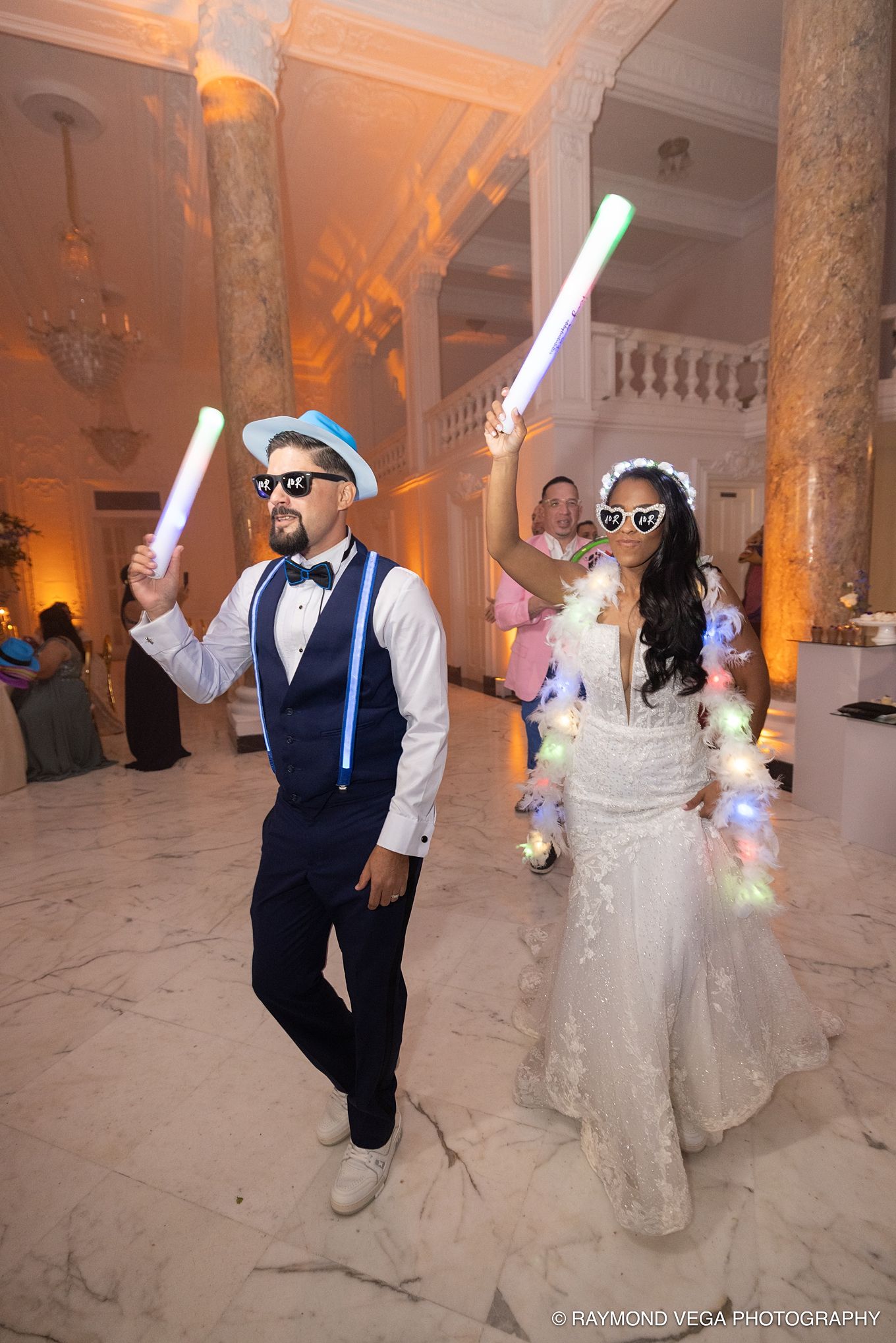 Bride and groom dancing with glowing sticks at elegant wedding reception, wearing fun sunglasses in grand marble ballroom.Antiguo Casino Pue