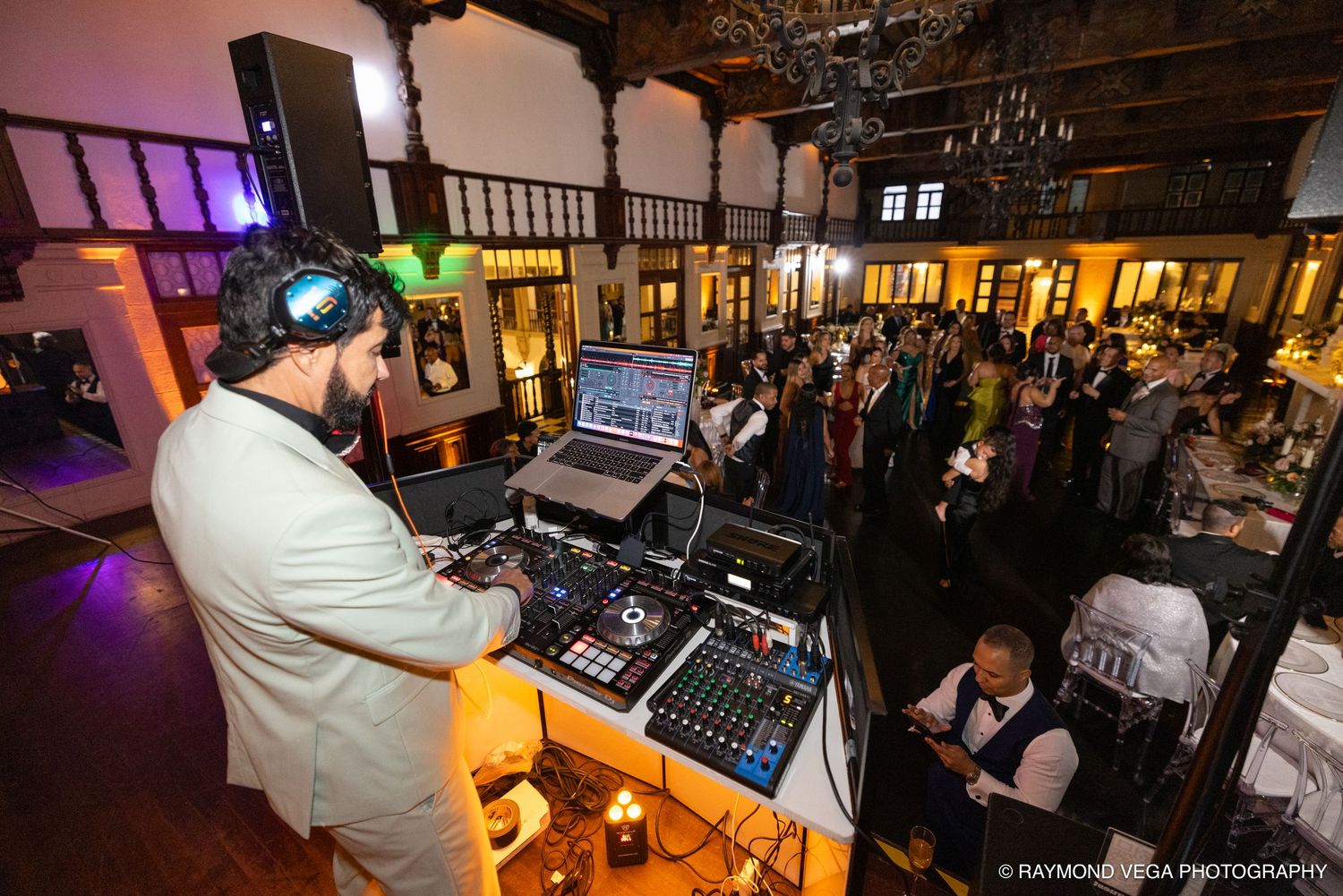 DJ performing at an elegant indoor wedding reception with guests dancing in a warmly lit venue.