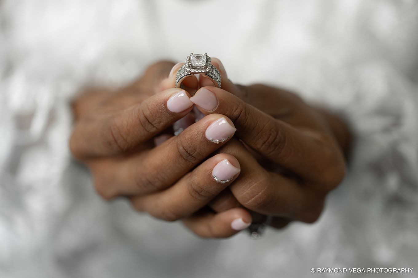 Close-up of a bride's hands with pink manicure holding a diamond halo engagement ring, photographed by Palomino Vega Photography.