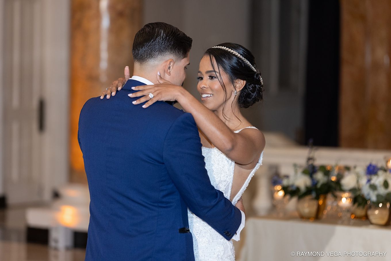 A bride and groom share their first dance, smiling joyfully in an elegant wedding reception venue.