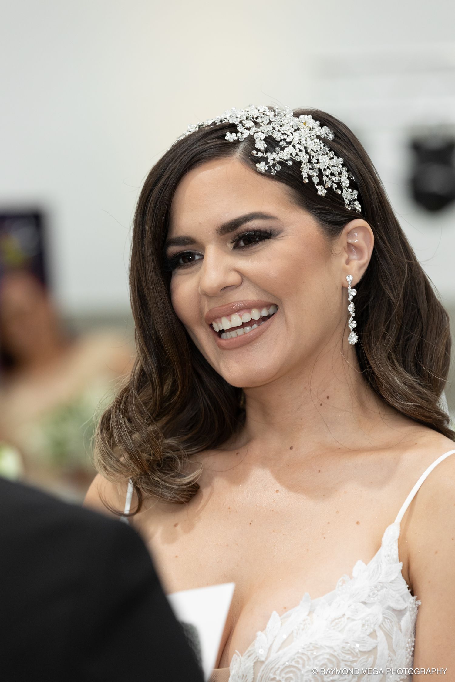 Smiling bride wearing a crystal hair accessory and drop earrings in a white lace wedding dress.