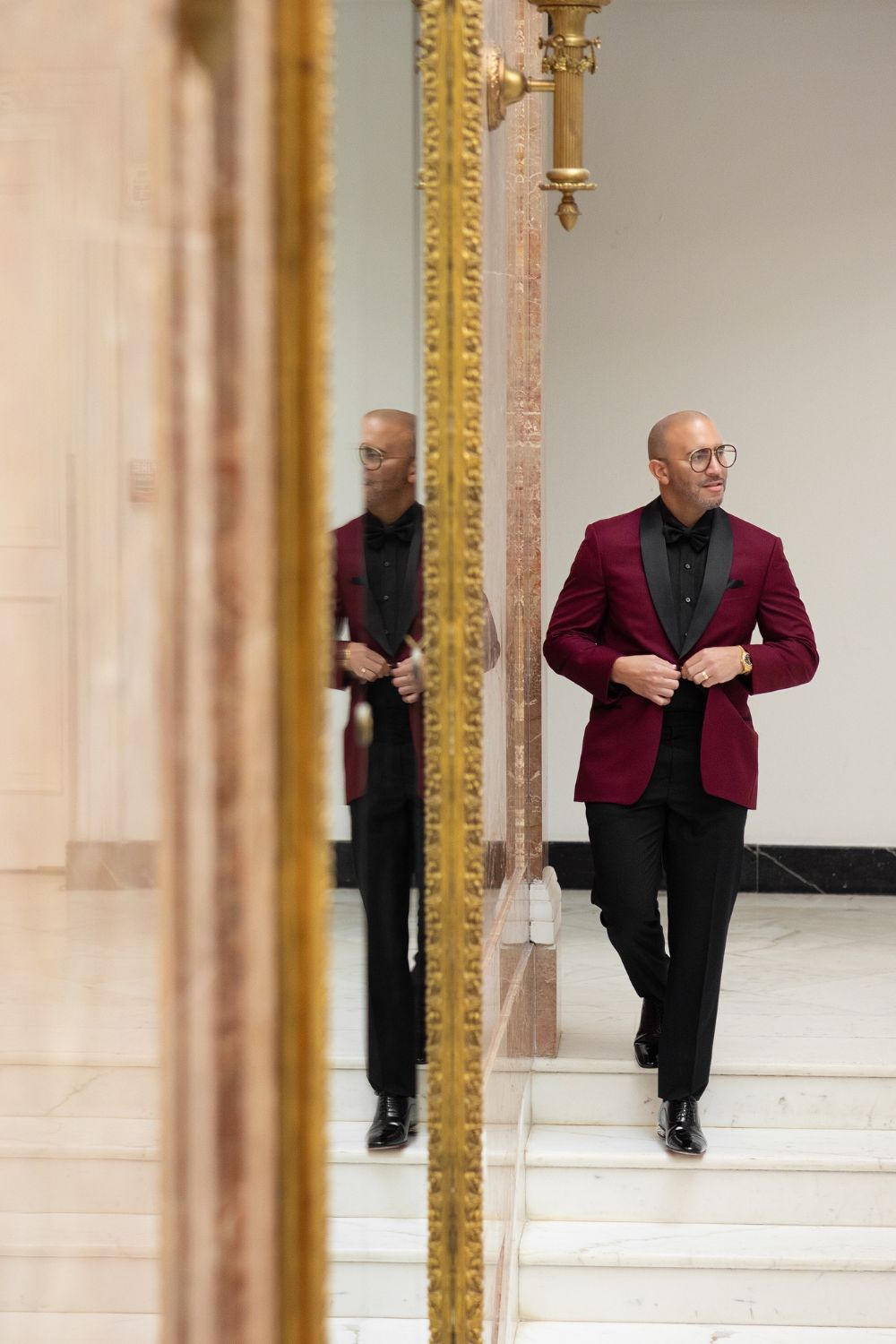 Bald man in burgundy blazer and black pants walks near ornate gold mirror in elegant interior. Antiguo Casino Puerto Rico