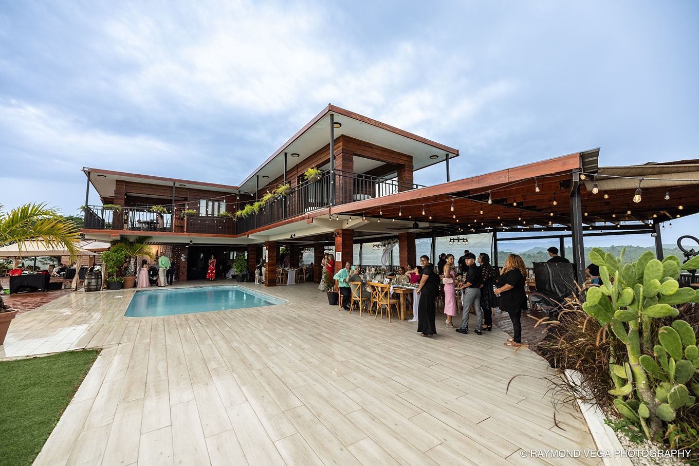Luxury villa with pool and guests gathered on patio during outdoor evening event with ocean views.