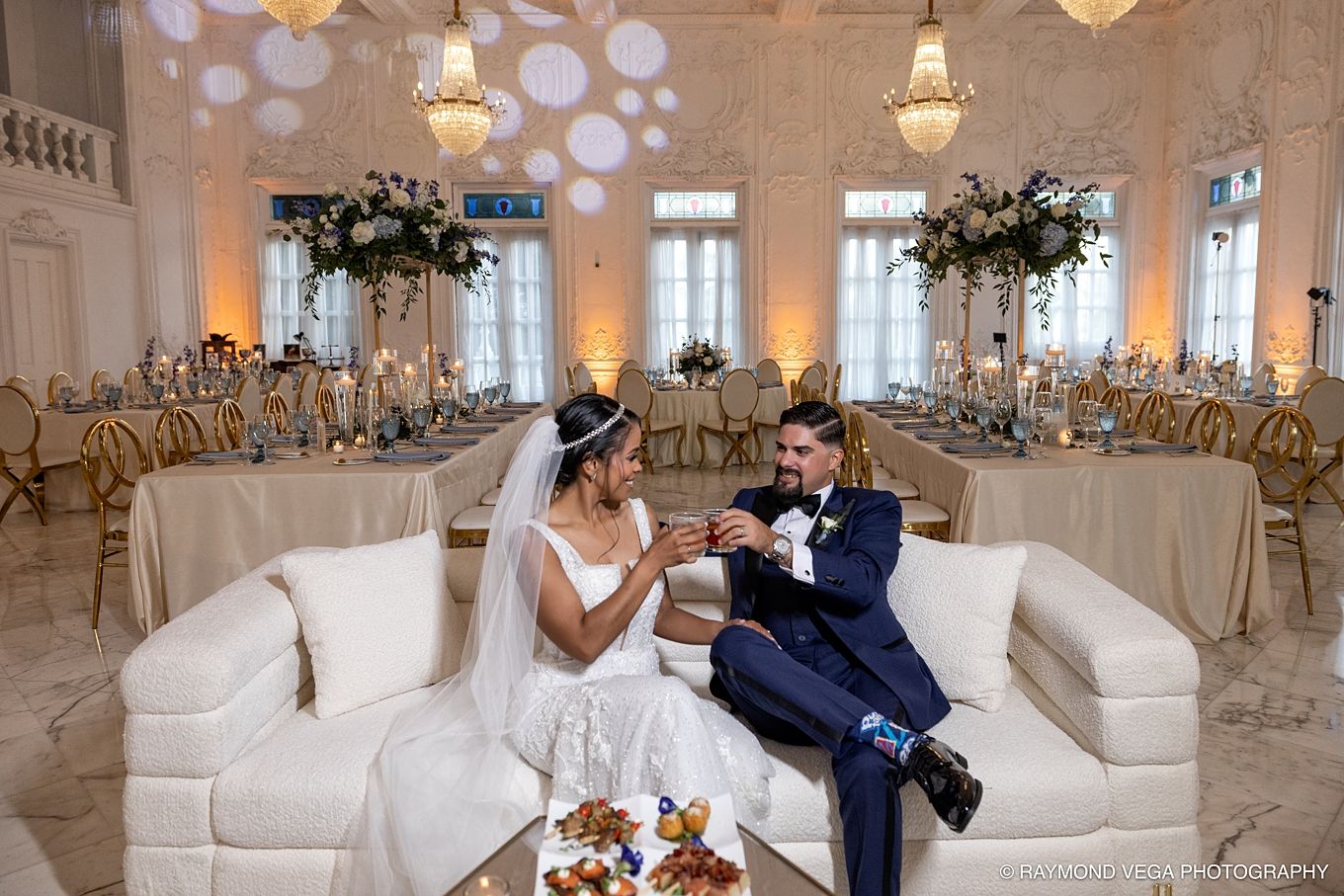 Bride and groom share a joyful moment on a white sofa in an elegantly decorated wedding reception hall. Antiguo Casino Puerto Rico wedding