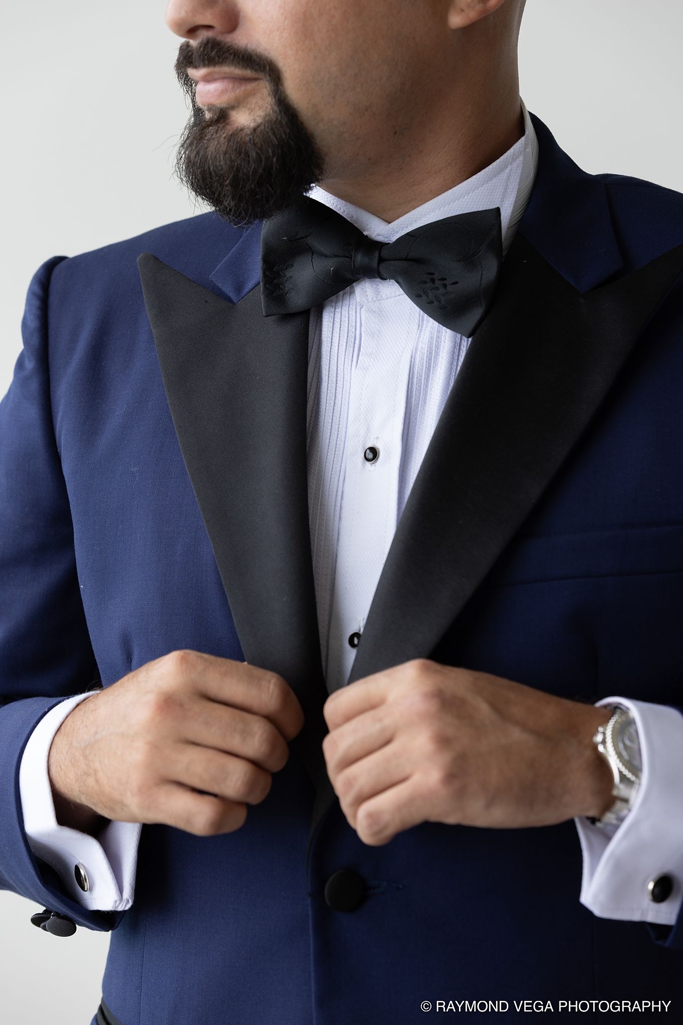 Man in blue tuxedo with black lapels and bow tie adjusting jacket, showcasing formal wedding attire. Hotel la Concha Wedding