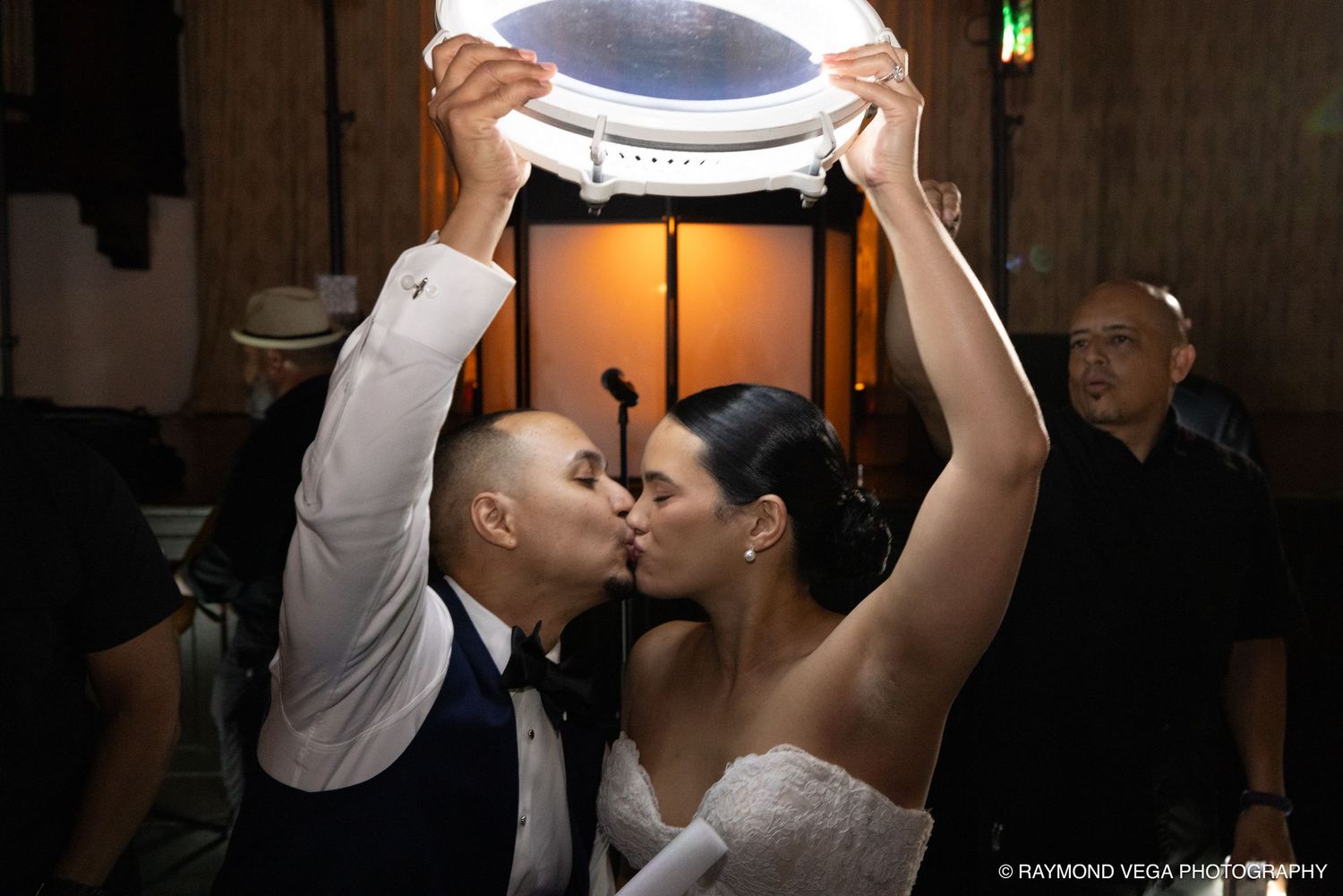 Bride and groom share a kiss under a decorative frame at their wedding reception.
