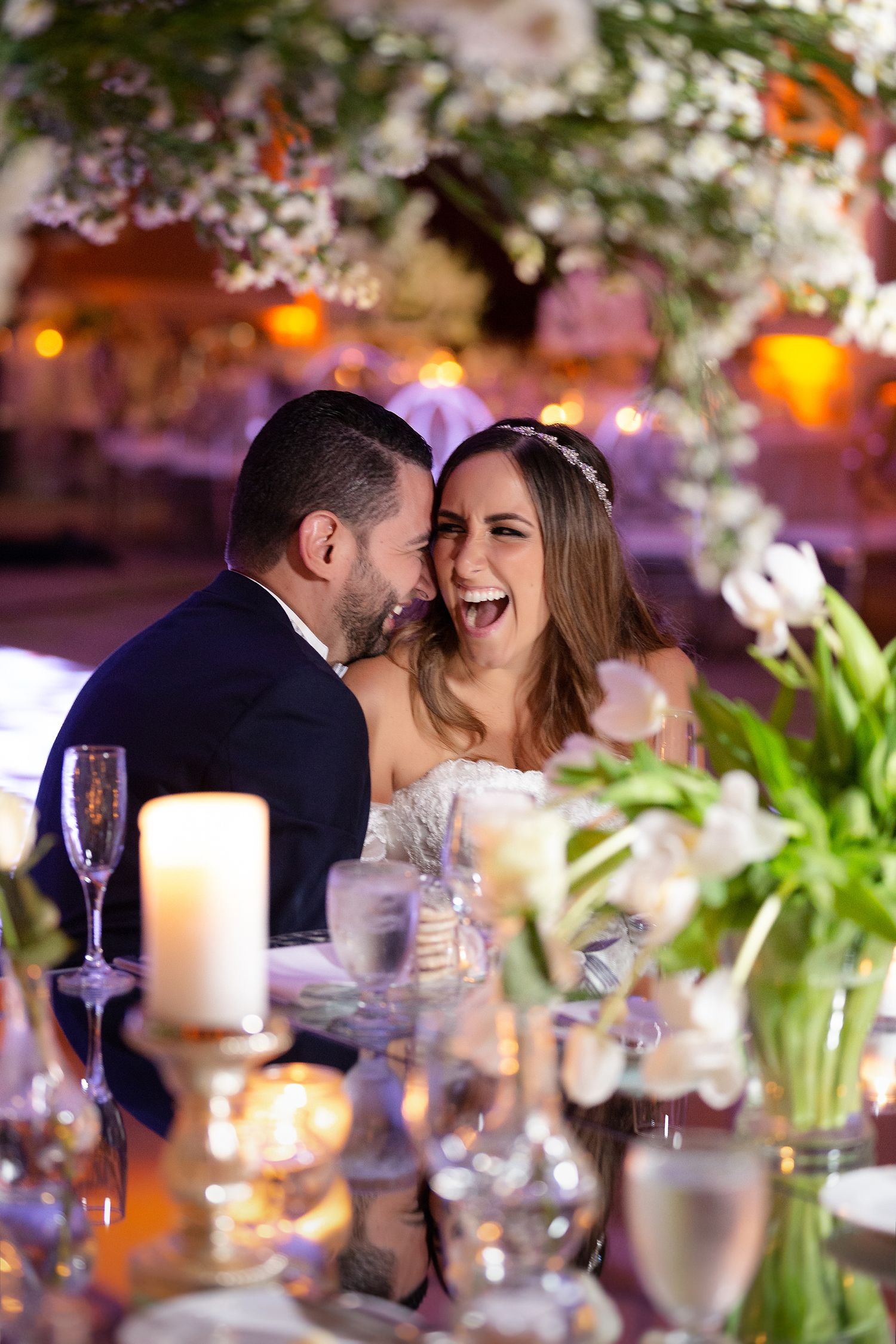 Joyful bride and groom laughing together at wedding reception table with candles and white floral arrangements. Marriott Hotel Puerto Rico
