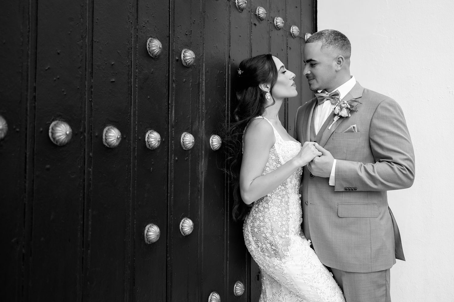 Black and white photo of a bride and groom sharing a romantic moment by an ornate wooden door. Raymond Vega Photography & Cinematography