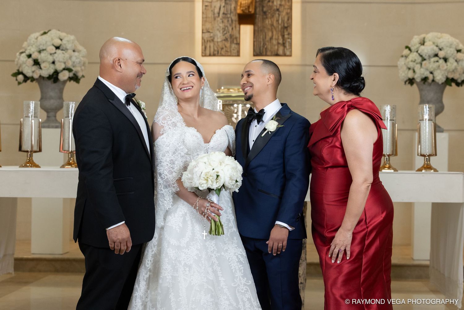 Bride and groom pose with family members in elegant wedding attire inside a beautifully decorated chapel.