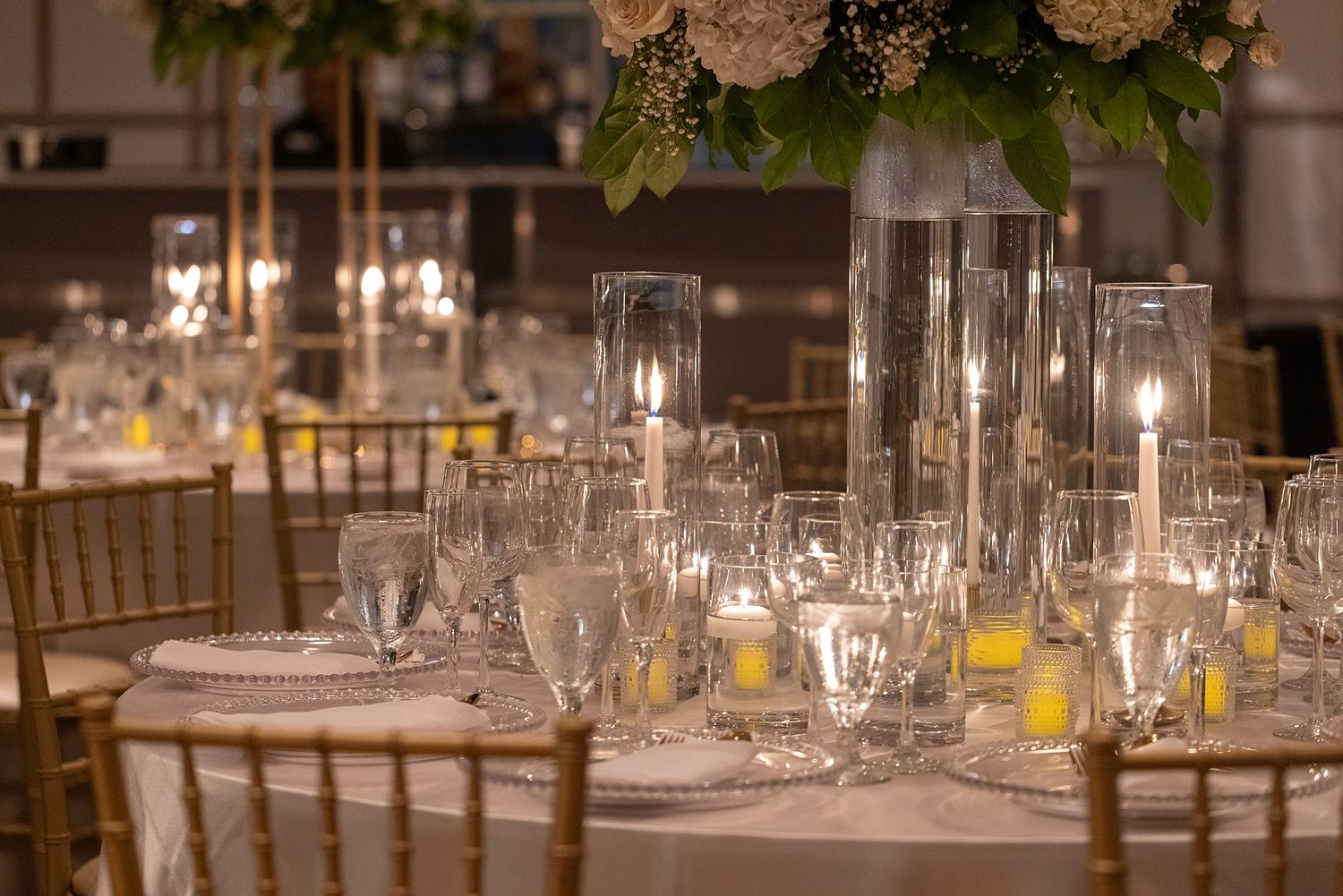 Elegant wedding reception table with crystal glassware, tall candles, and floral centerpieces on white linen.