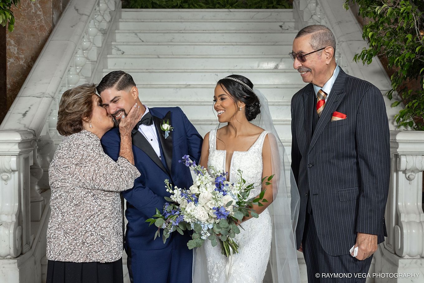 Bride and groom share a joyful moment with family on elegant marble stairs during a wedding celebration.