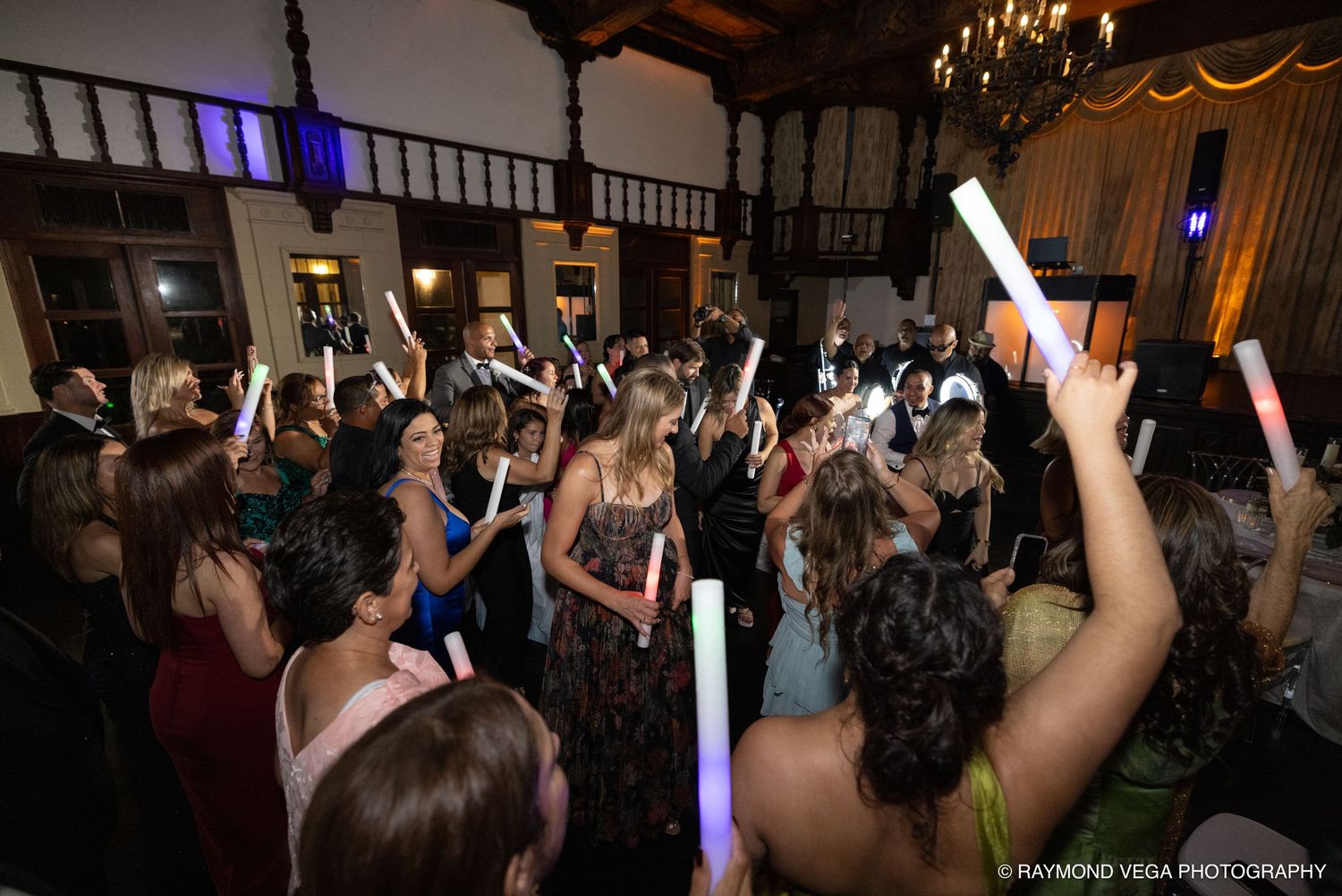 Guests dancing and holding glowing foam sticks at an elegant indoor wedding reception party.