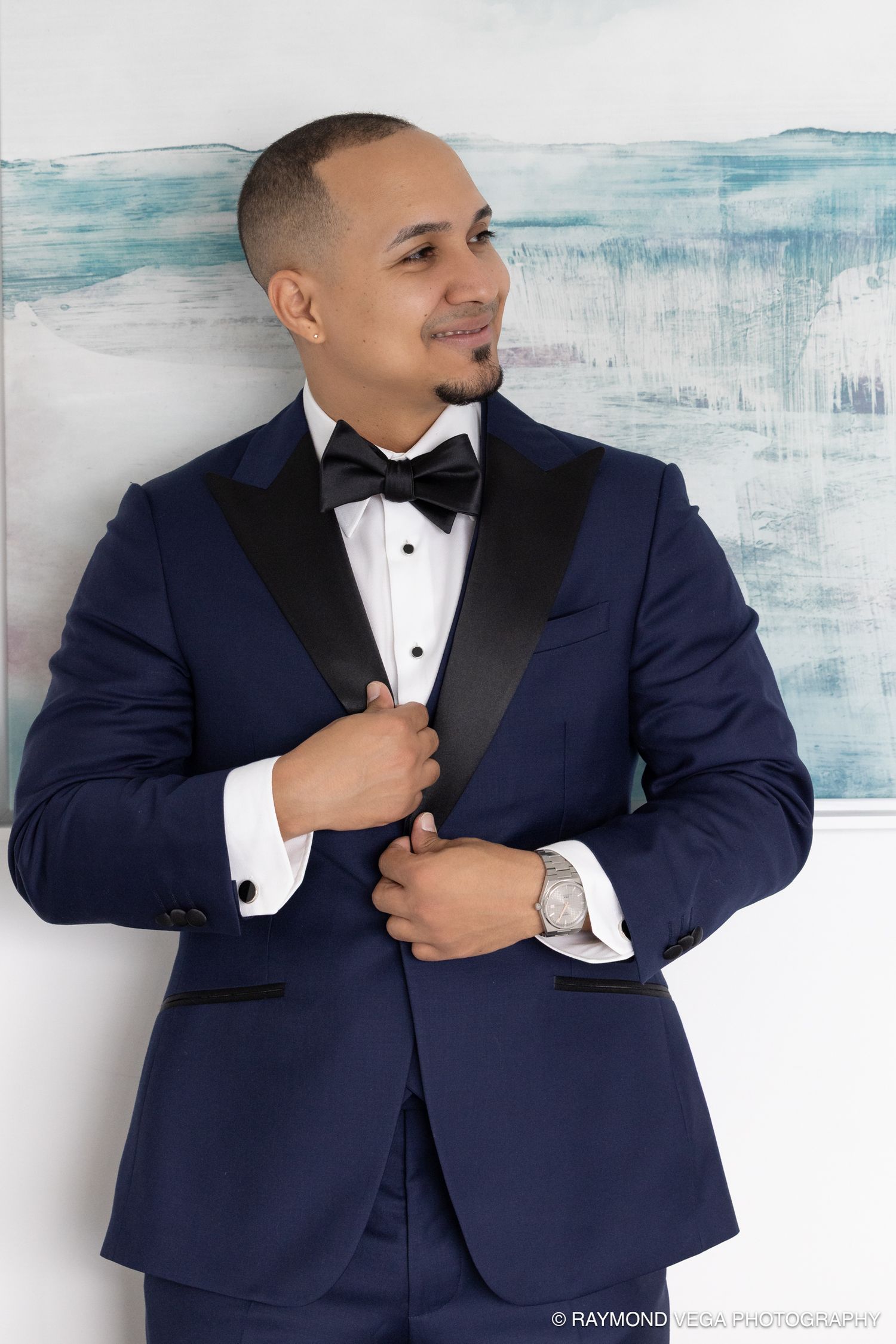 Man in navy blue tuxedo with black lapels and bow tie smiling confidently in a formal portrait photo.