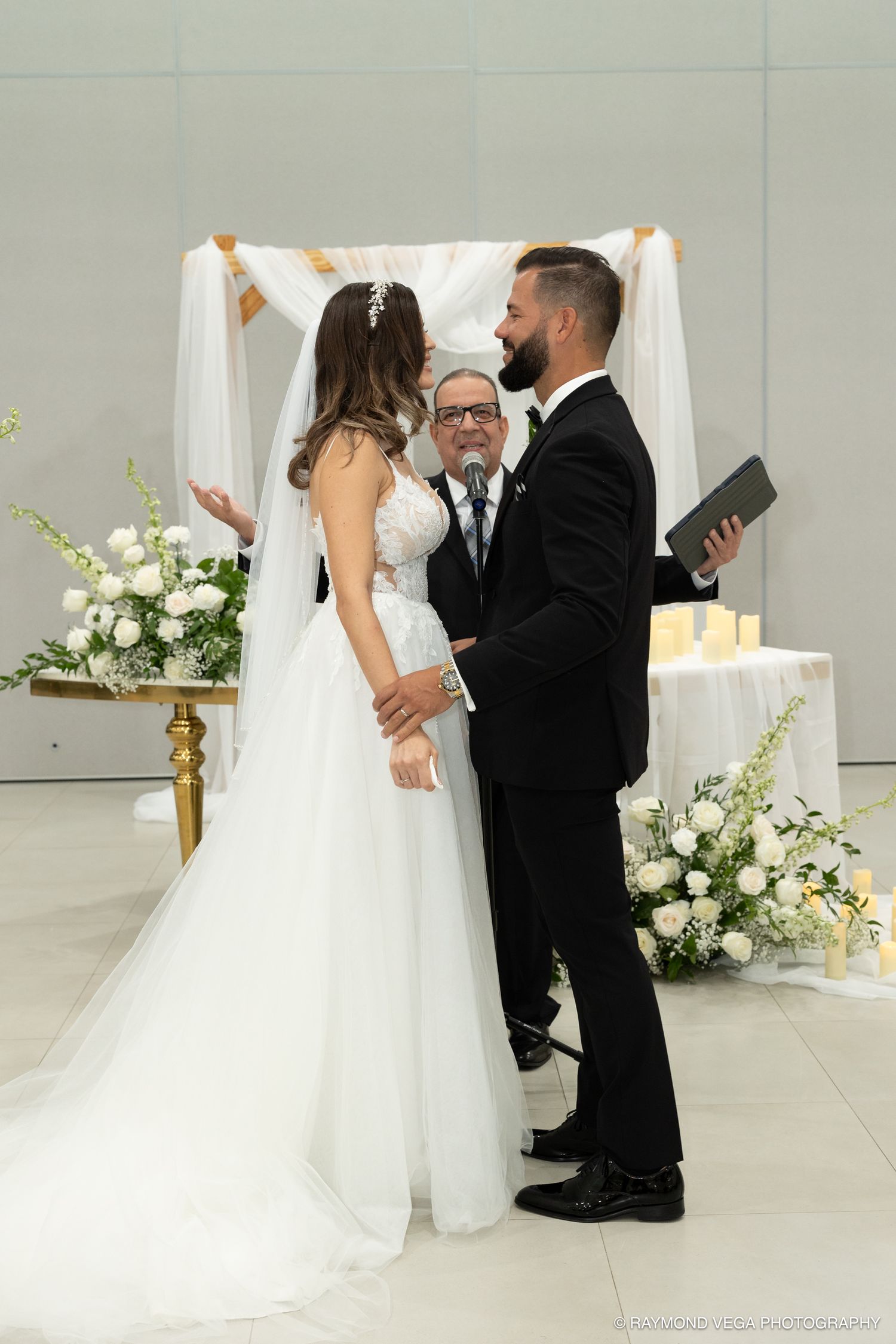 Bride and groom exchange vows under a chuppah with white floral arrangements during an elegant wedding ceremony.