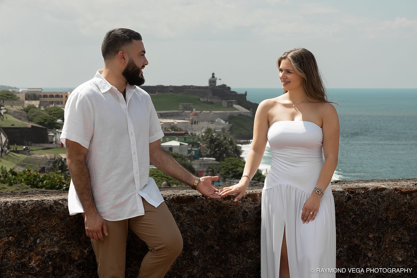 Couple holding hands in white outfits with El Morro fort and Caribbean Sea in background, San Juan Puerto Rico.