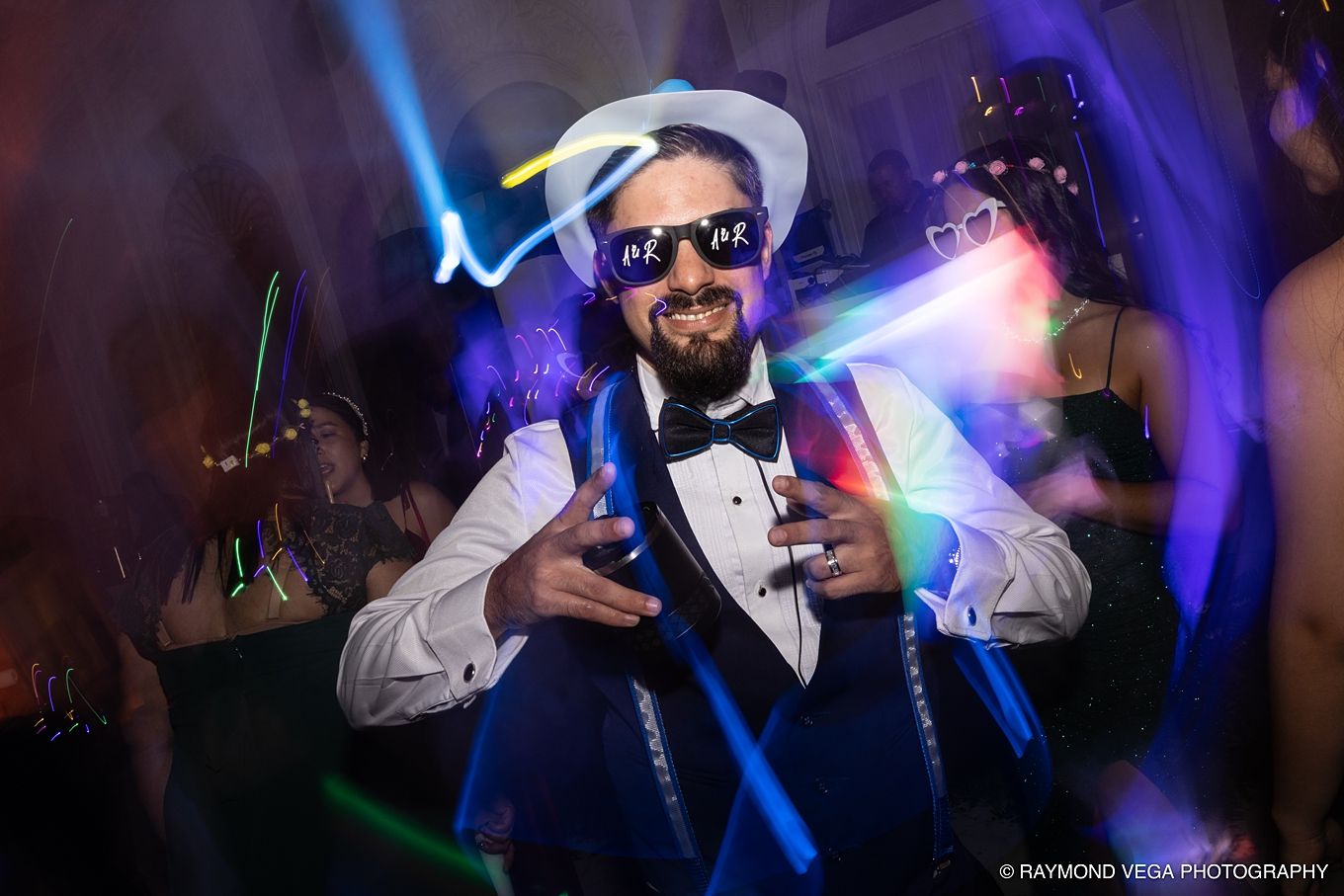 Man in white fedora and LED sunglasses dancing at a neon-lit party in a blue tuxedo. Antiguo Casino Puerto Rico wedding