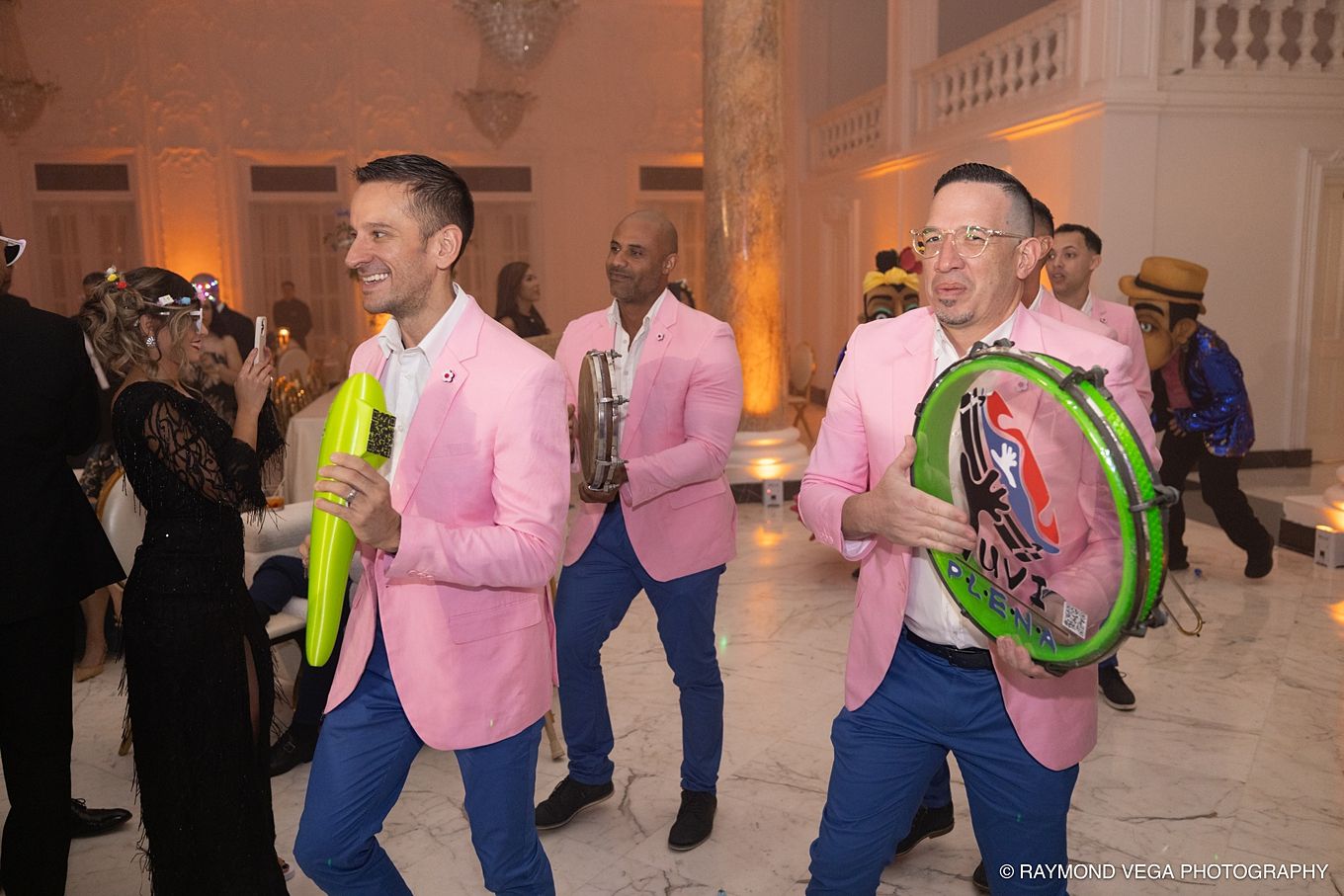Men in pink blazers and blue pants play colorful instruments at a festive indoor celebration PLENEROS EN PUERTO RICO