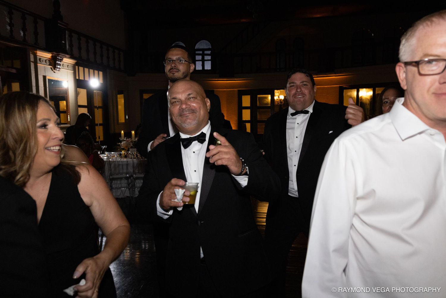 Guests in formal attire socializing at an elegant evening gala event, man in tuxedo smiling holding a drink.