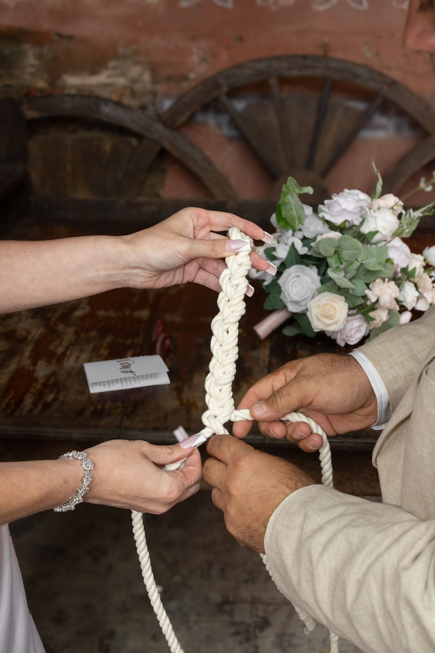 Couple tying a unity knot ceremony rope braid at rustic wedding with floral bouquet in background. Gallery Inn Puerto Rico