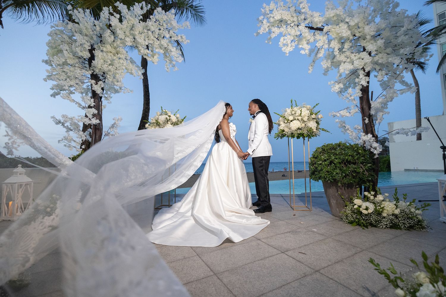 Bride and groom exchange vows at an elegant outdoor wedding ceremony with white floral arches and ocean views.