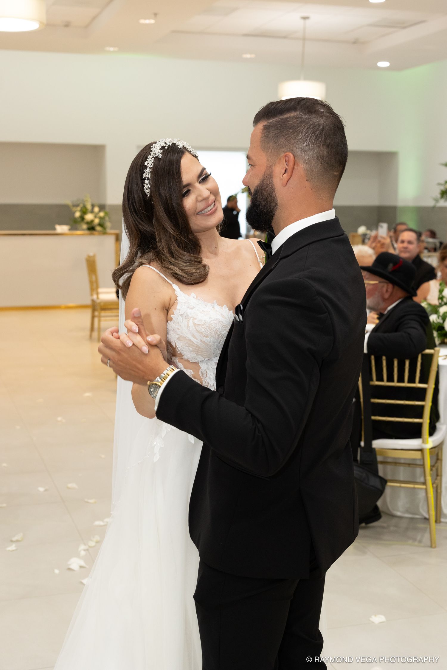 Bride and groom share their first dance at wedding reception, bride smiling in white gown, groom in black suit.