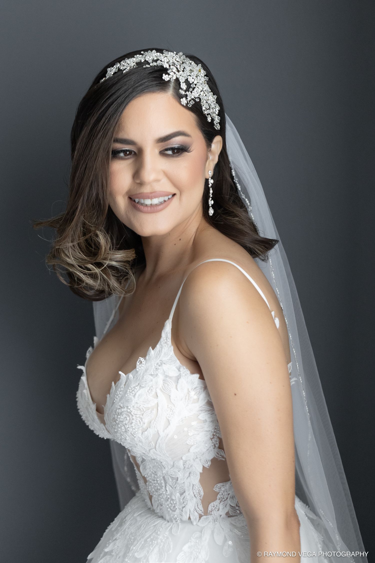 Smiling bride in lace wedding gown with floral headpiece and veil poses for bridal portrait photo.
