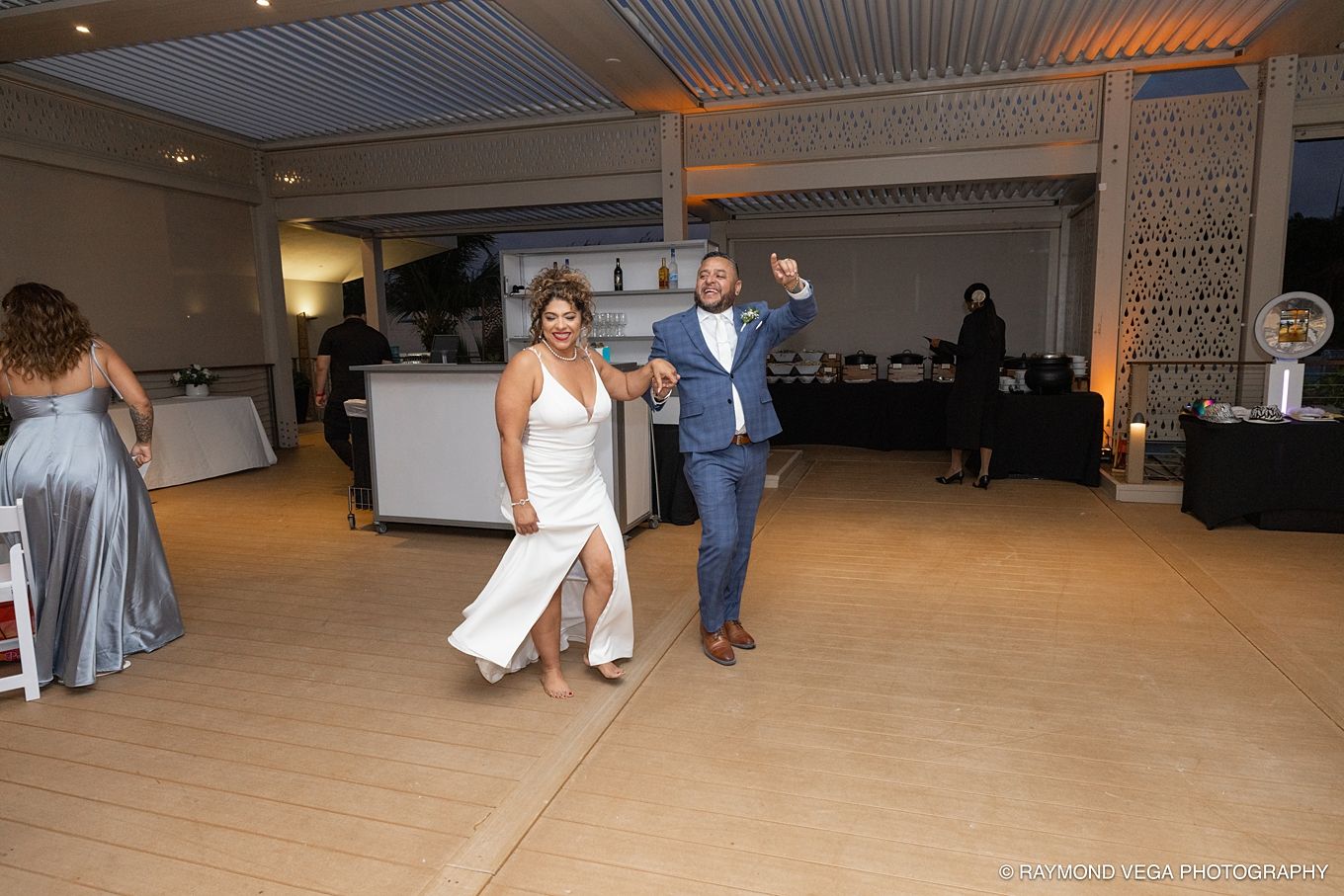 Bride and groom dancing joyfully at their wedding reception on a dance floor surrounded by guests.