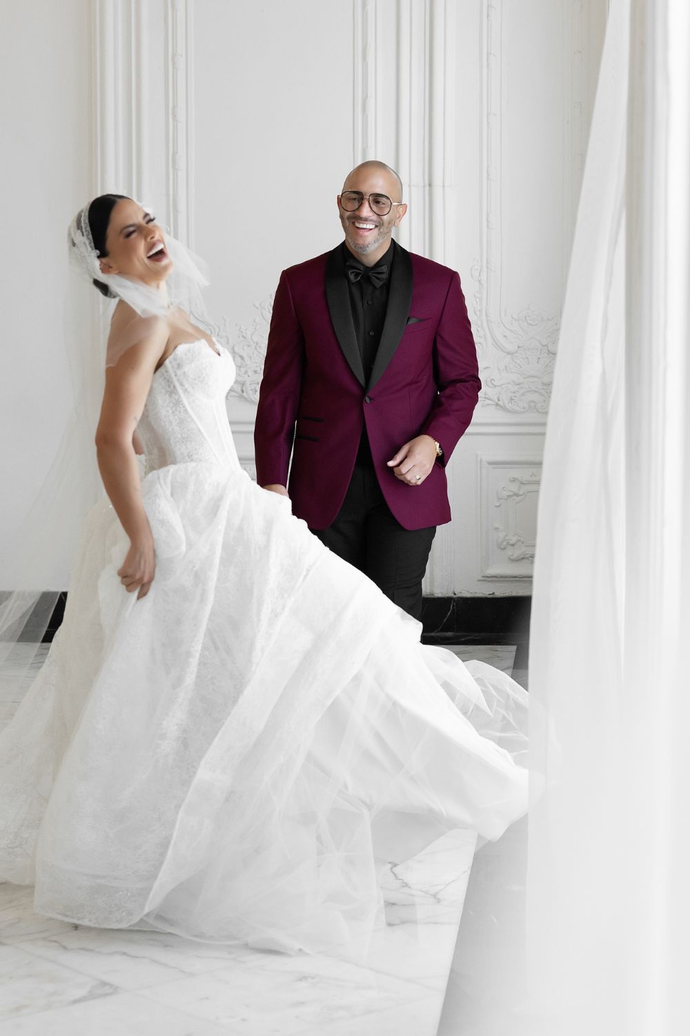 Bride in white ballgown laughing with groom in burgundy tuxedo jacket on marble steps. Antiguo Casino Puerto Rico