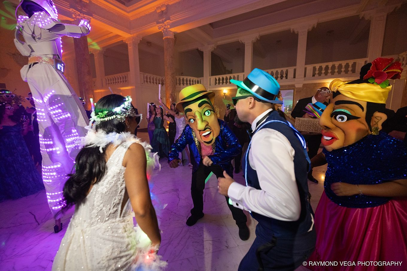 Lively wedding reception with guests dancing in colorful masks and costumes under warm ballroom lighting. PLENA EN PUERTO RICO