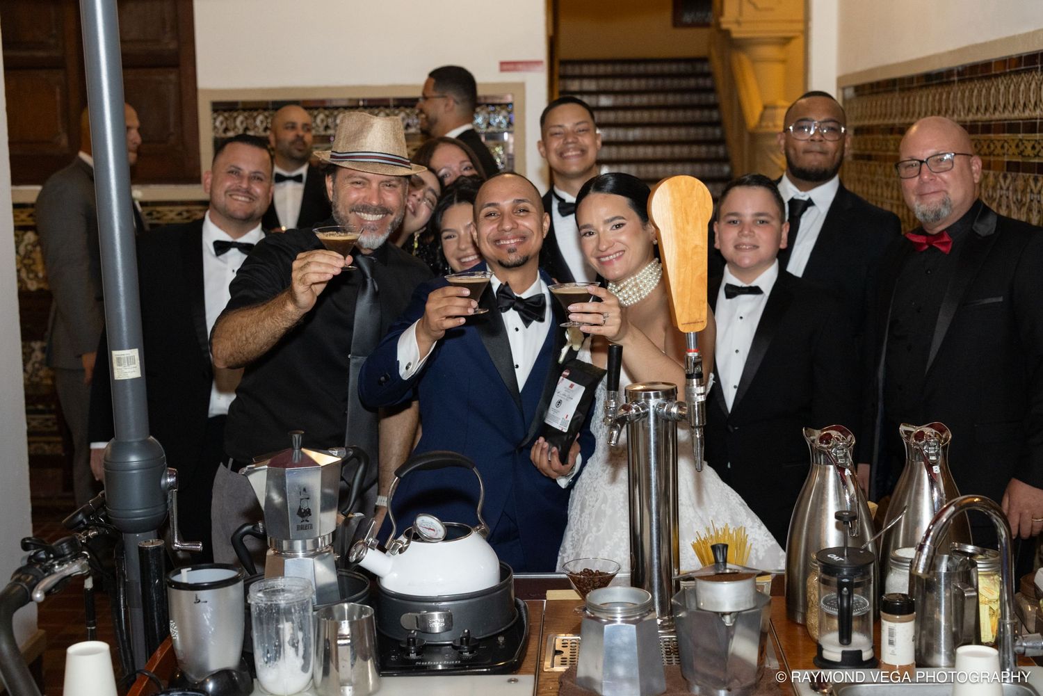 Group of elegantly dressed people posing and toasting at a bar during a formal event or wedding reception.
