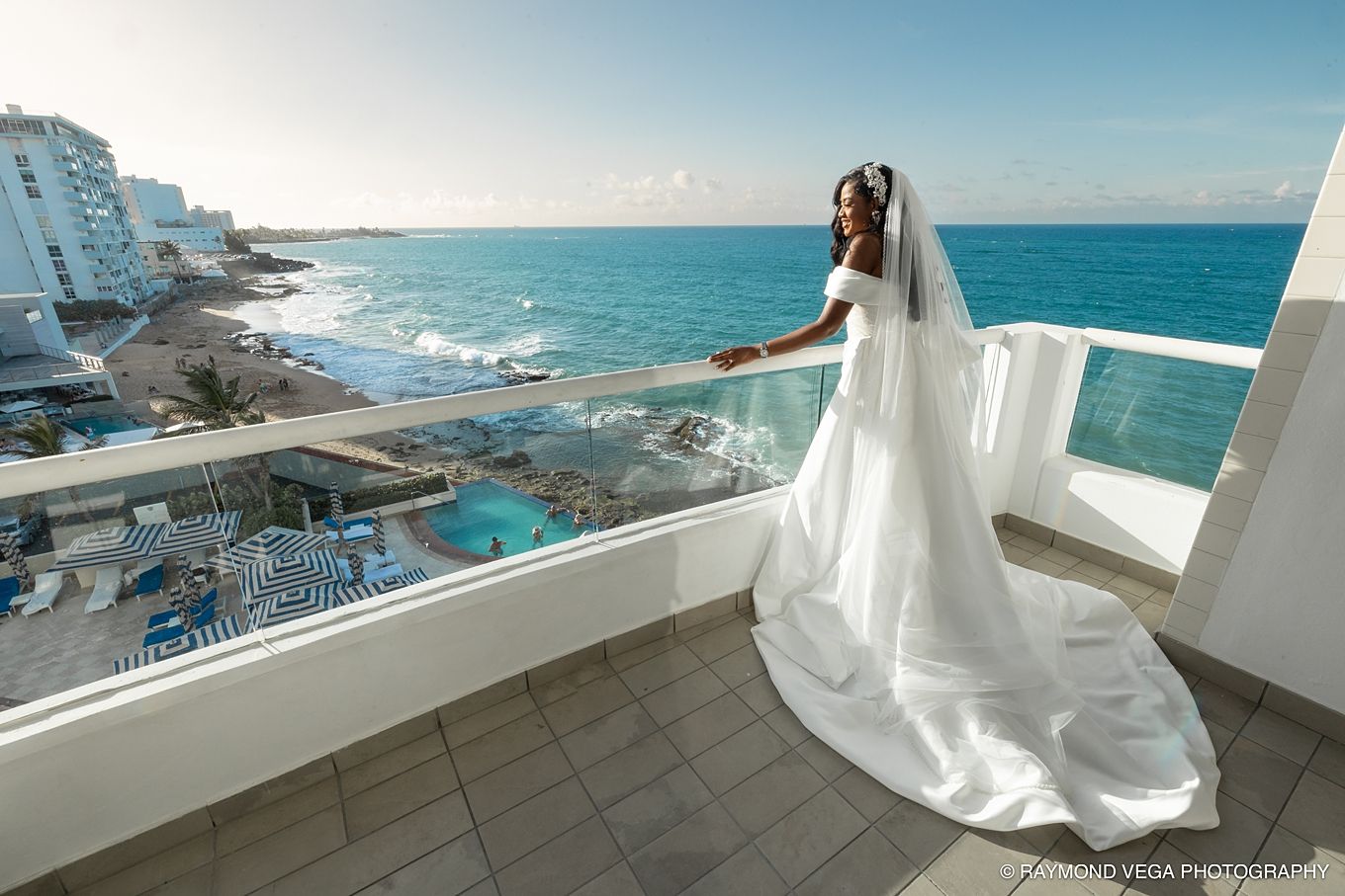 Bride in white gown and veil poses on ocean-view balcony at Cancun resort on her wedding day. Hotel Condado Vanderbilt Puerto Rico