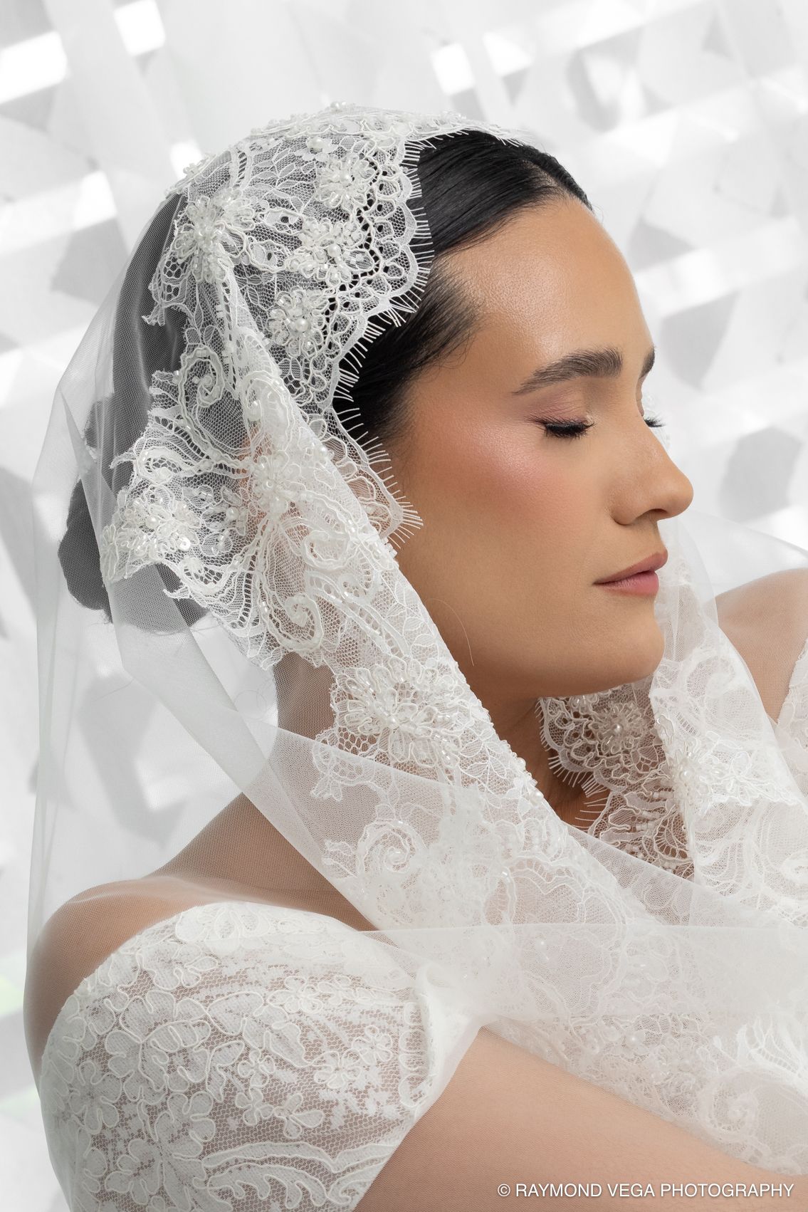 Bride in elegant lace wedding dress and veil with eyes closed, captured by Raymond Vega Photography.