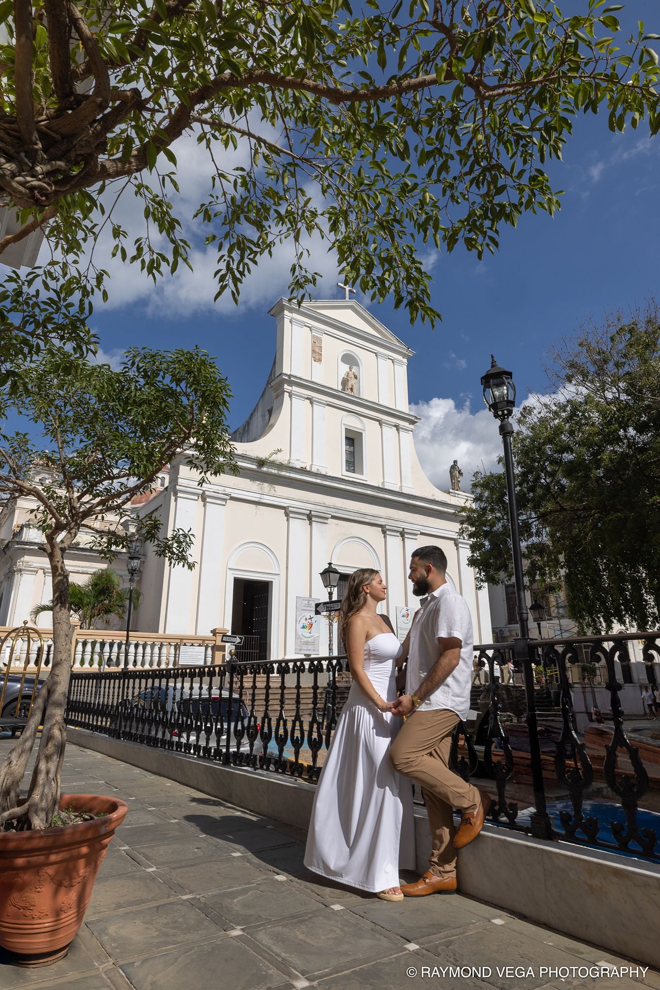 Couple in white attire poses before a historic white church in Old San Juan, Puerto Rico on a sunny day.  Love Story Photos
