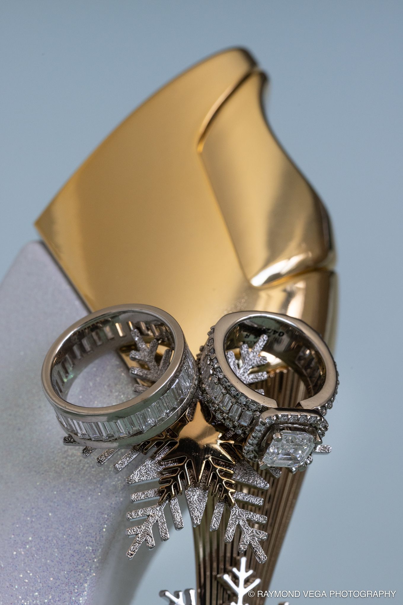 Two diamond wedding rings displayed on a snowflake ornament with a gold backdrop by Raymond Vega Photography. Hotel la Concha Wedding