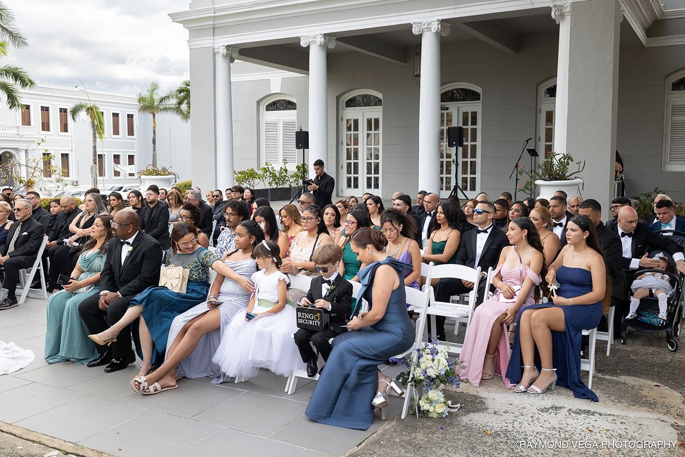 Guests seated outdoors at an elegant wedding ceremony in front of a white colonial mansion. Antiguo Casino Puerto Rico