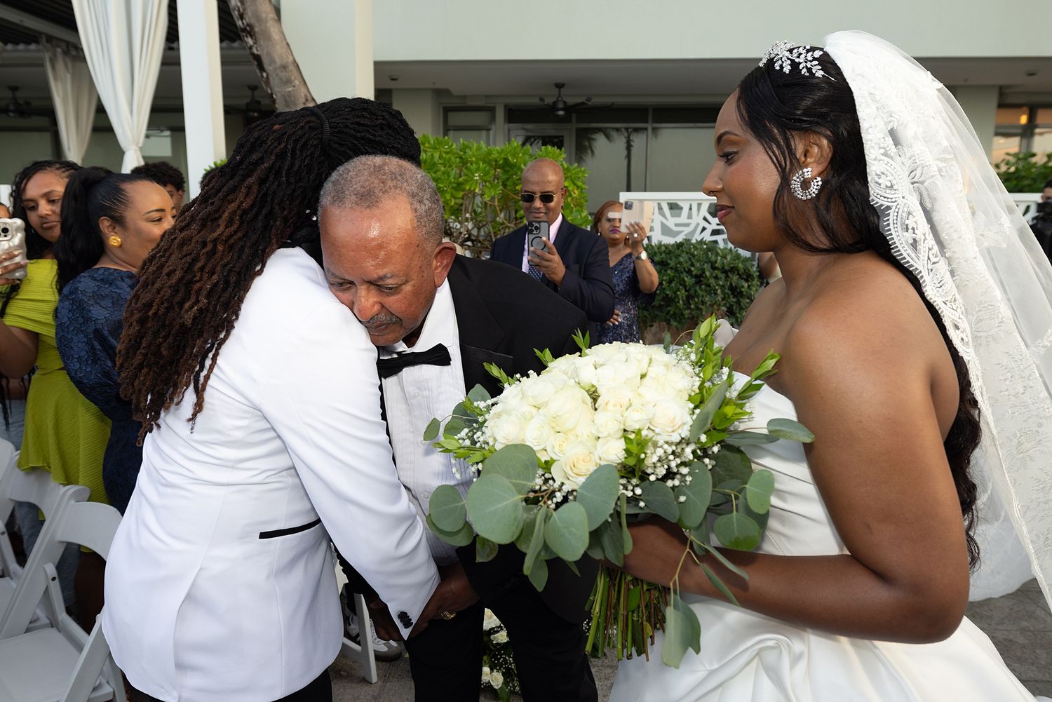 A bride in a white gown and veil receives her bouquet of white roses during an outdoor wedding ceremony. Hotel La Concha Puerto Rico